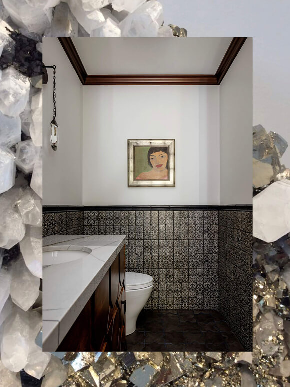 Powder room with patterned wall tile, dark wood vanity, marble top, and framed vintage-style portrait.