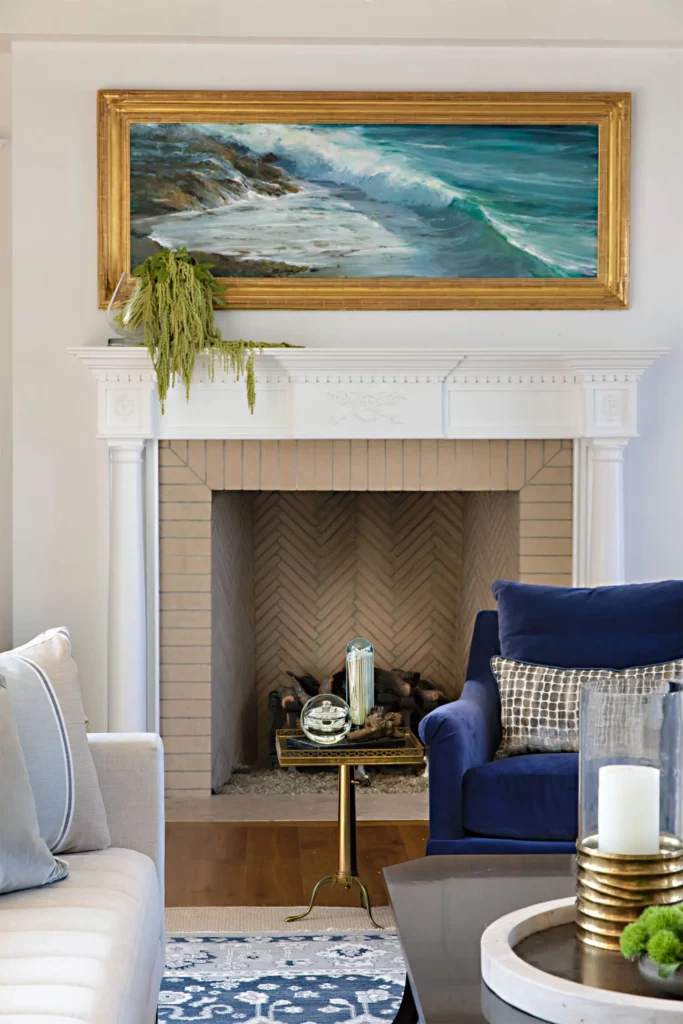 Cozy living room with herringbone tile fireplace, seascape art, blue chair, and metallic glass decor by Grace Blu.