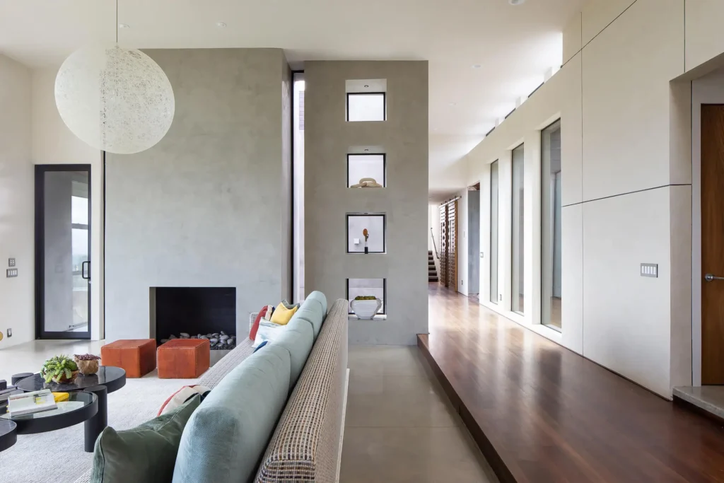 Interior of a house designed by Grace Blu. Living room with concrete walls in the living room, hard wooden floors in the hallway. Tall windows and doors
