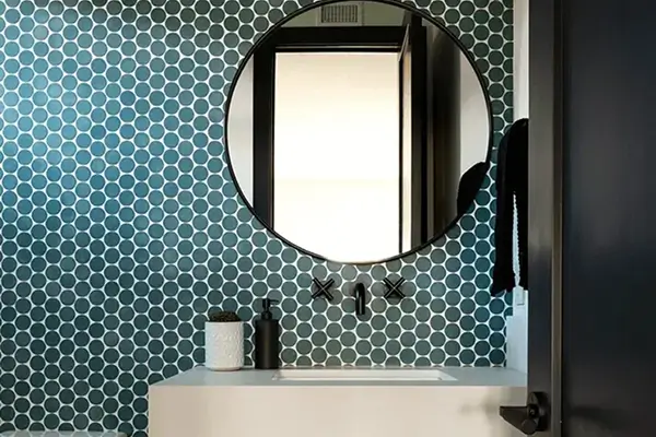 Contemporary bathroom by Grace Blu with teal tile, round mirror, wood vanity, and matte black fixtures.