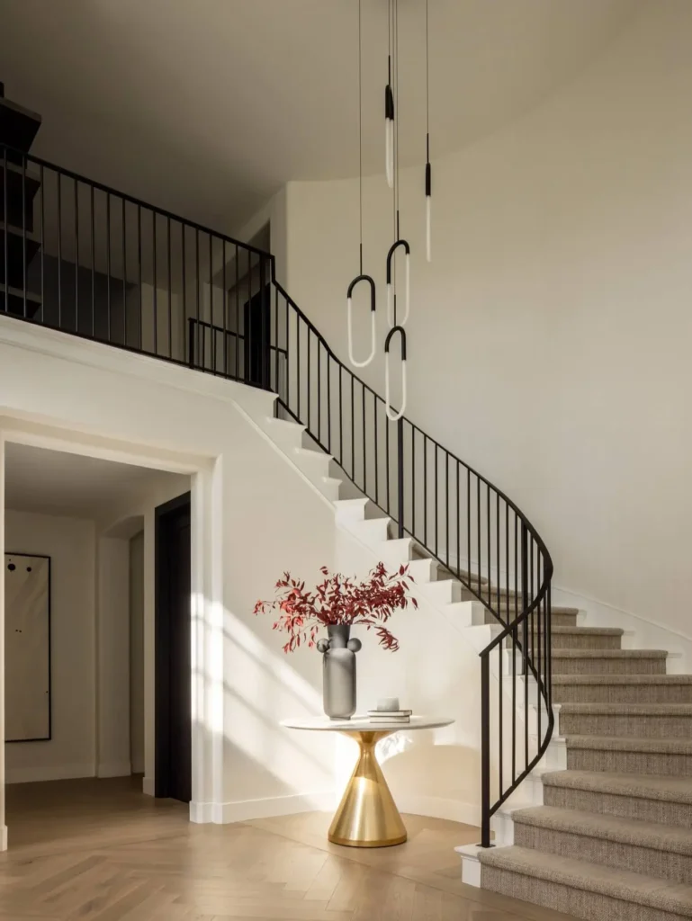 Elegant Grace Blu entryway with curved stair, iron railing, pendant light, and marble table with red foliage centerpiece.
