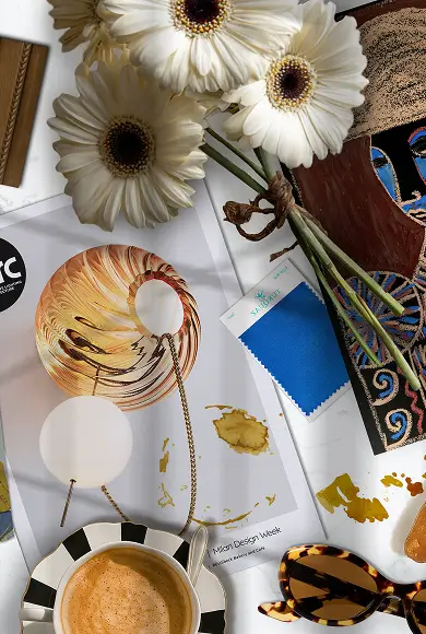 Flat lay with daisies, espresso, bold blue fabric swatch, sunglasses, and artistic design inspiration pieces.