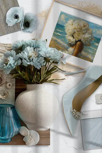 Flat lay with soft blue florals, seashells, coastal artwork, and an elegant light blue heel.