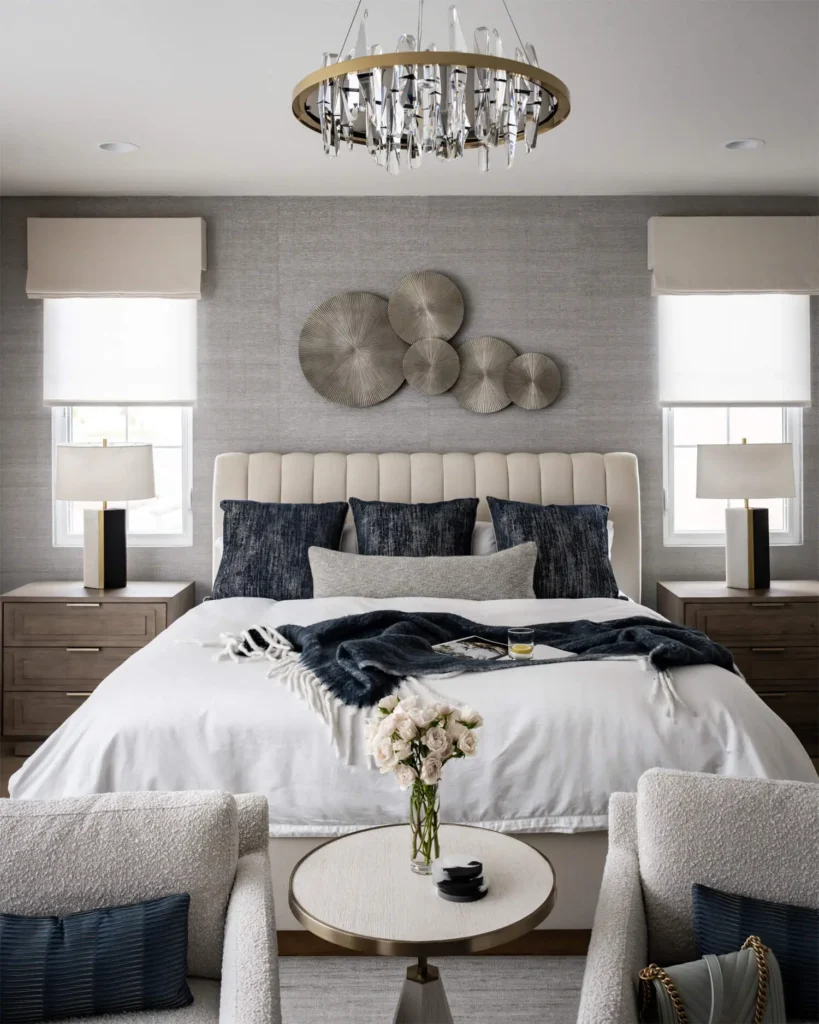 Modern bedroom with tufted headboard, neutral bedding, navy accent pillows and metallic wall sculpture above bed, designed by Grace Blu Interior Design.