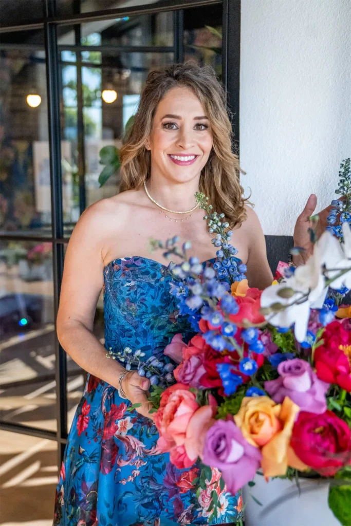Woman wearing strapless blue floral gown with vibrant bouquet of multicolored roses smiling at Grace Blu event.