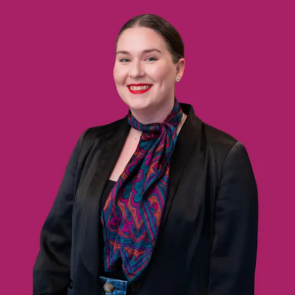 Katie, a designer at grace blu design wearing a scarf and smiling in front of a magenta background