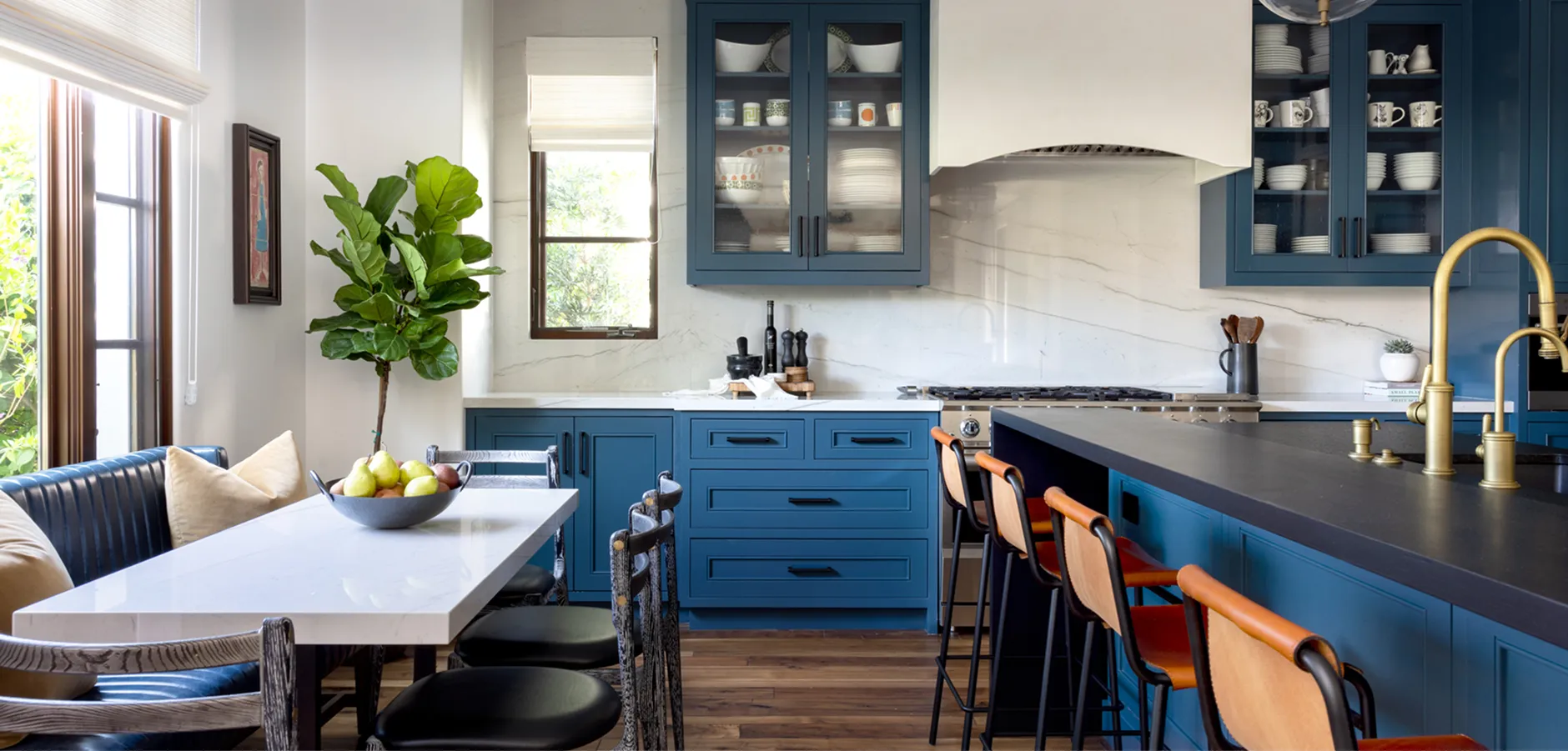 Spacious kitchen with white marble surfaces, blue cabinets and seating, and natural light from large windows.