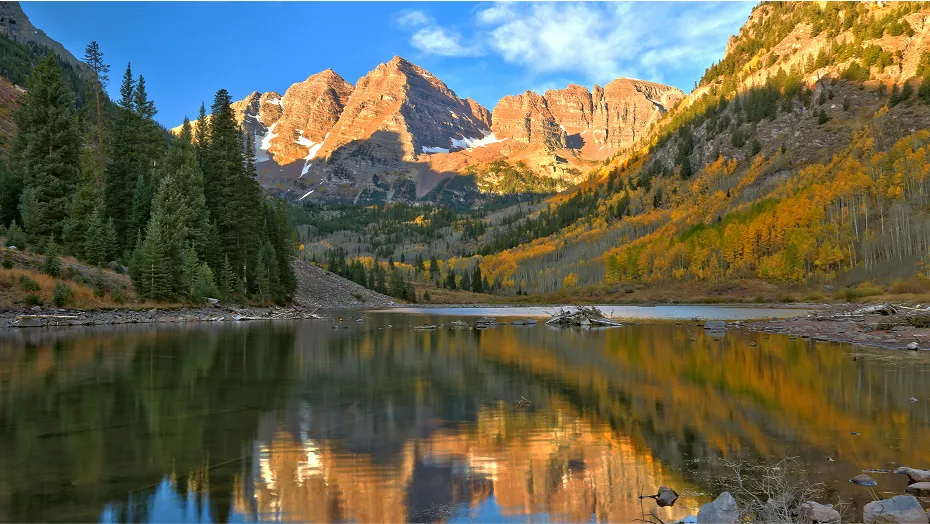 A landscape featuring mountains with colorful trees and a beautiful reflective lake in the foreground