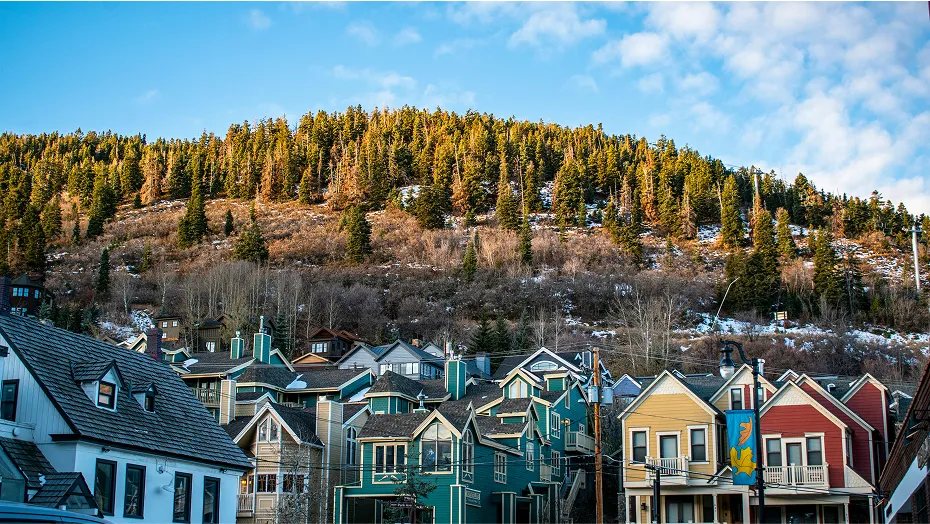 View of the tall, colorful houses in Park City with green pine trees in the mountains just behind them