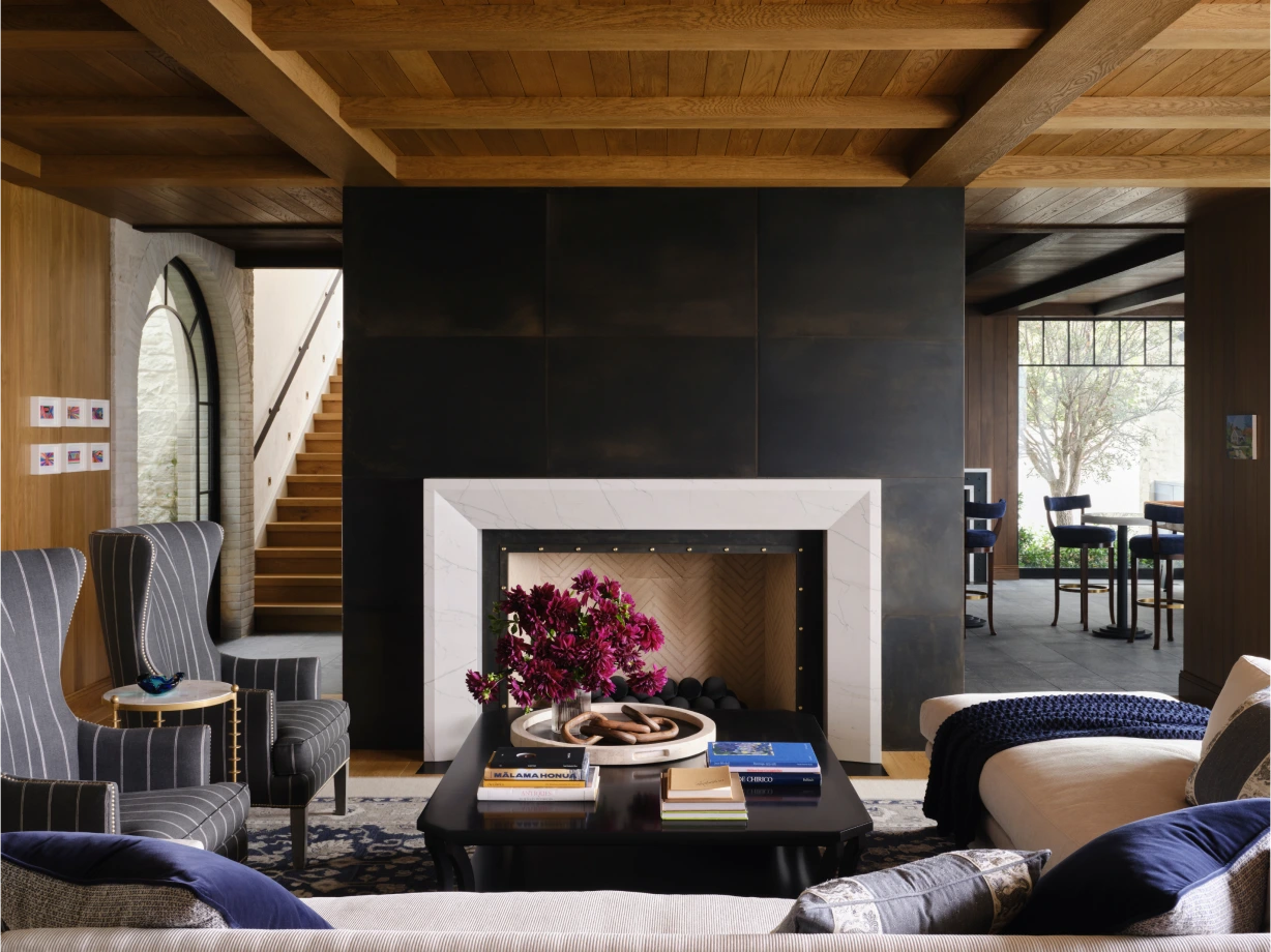 Moody living room with dark beams, large black fireplace, neutral sofas, and built-in banquette.
