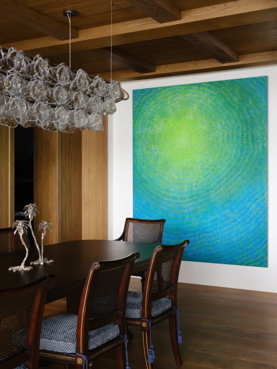 Dining room with large blue abstract art, crystal chandelier, dark wood table and wicker chairs, designed by Grace Blu Interior Design.