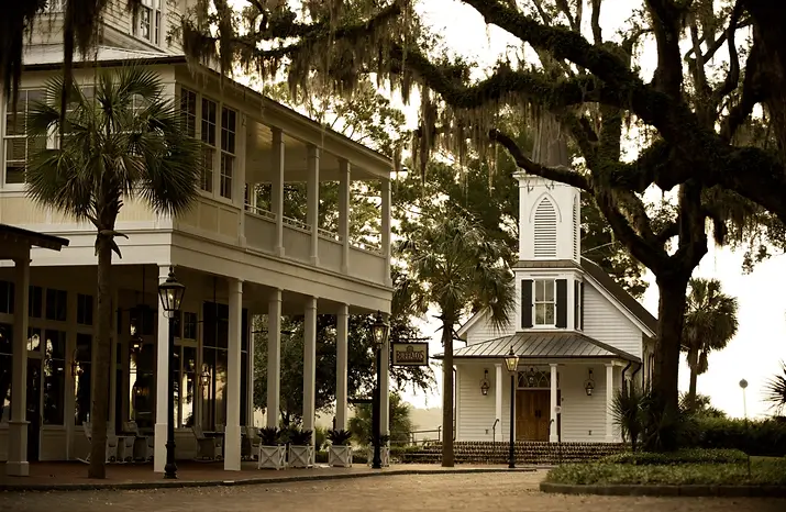 Southern-style plantation house exterior with palm tree, deep porch and oak draped in Spanish moss, representing Grace Blu lifestyle inspiration.