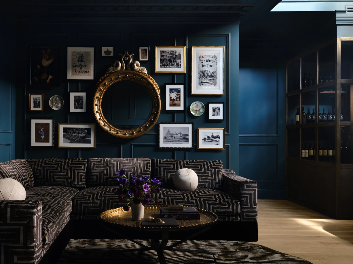Dramatic black and gold living area with gallery wall, round gold mirror and dark patterned couch with brass coffee table
