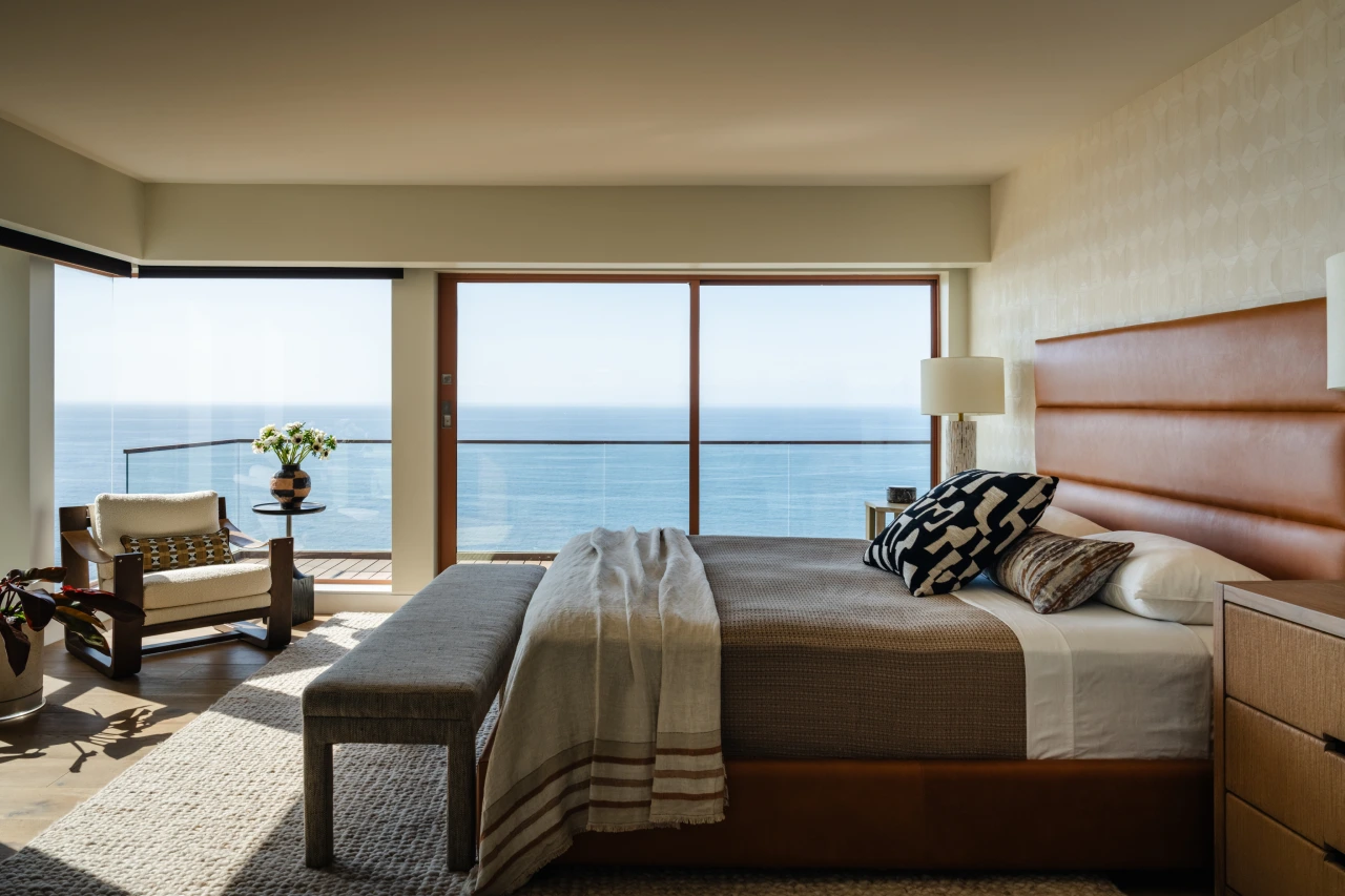 Modern coastal bedroom with ocean view, leather bed, earthy tones, textured fabrics, and minimalist decor.