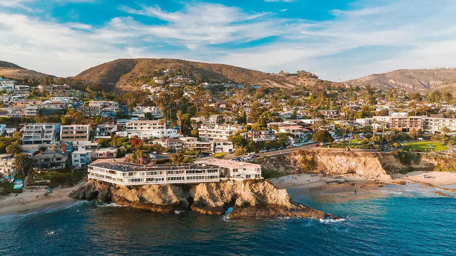 Aerial view of Laguna Beach, CA coastline featuring rocky cliffs and hillside homes at sunset, captured for Grace Blu Interior Design