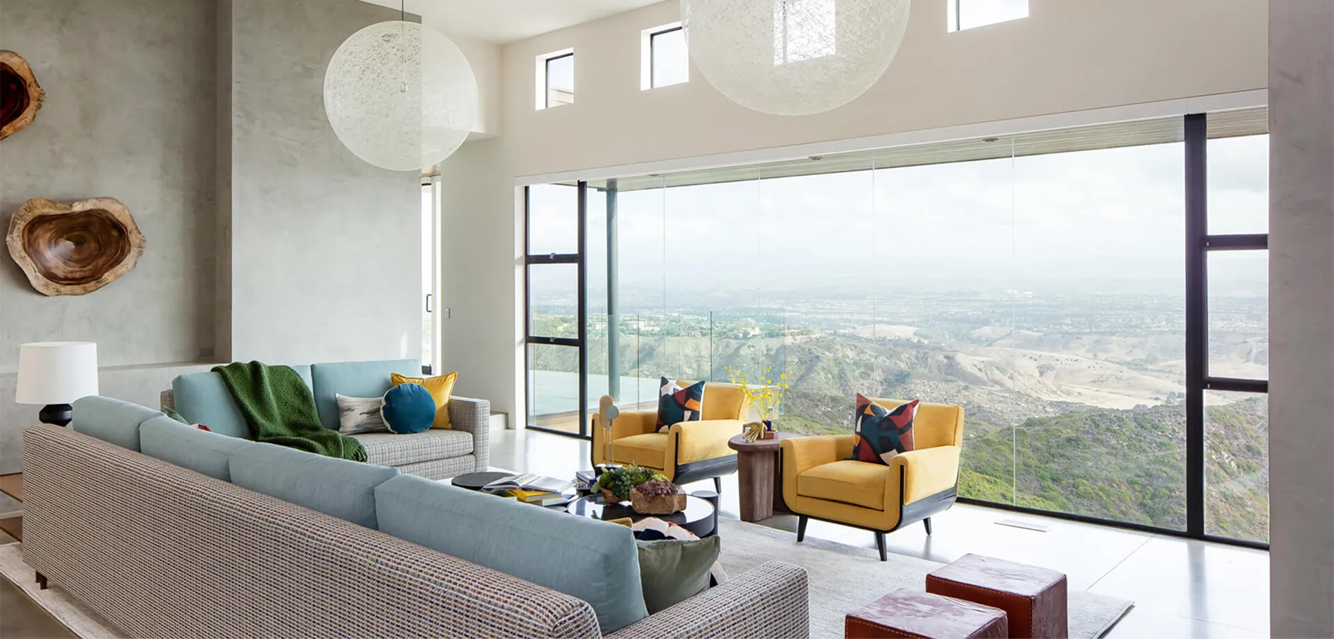 Colorful living room with green chairs, blue sofa, and valley view through tall windows.