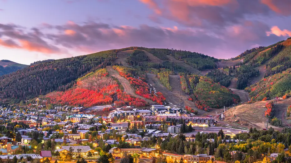 Park City sunset with glowing city lights, ski lifts, and fall-colored trees.
