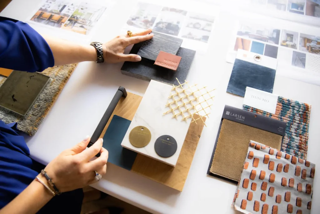 A Grace Blu designer reviews a curated flat lay of material samples, hardware, and fabric swatches during the design planning process, showcasing a mix of textures, finishes, and color palettes.
