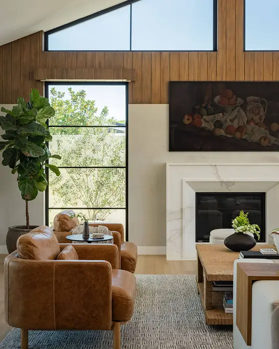 A modern living room with a vaulted ceiling and a fireplace. Brown leather chairs and a white sectional sofa are arranged around a coffee table.