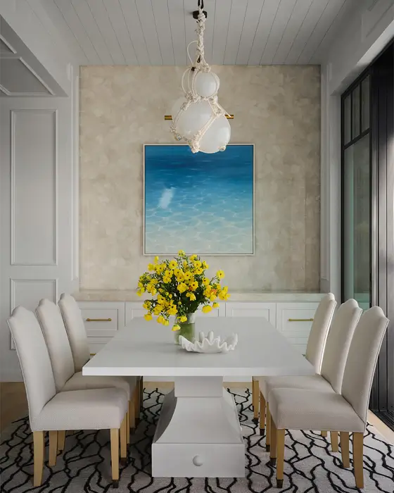 Dining room with metallic wallpaper and ocean art, chandelier over floral on white table with cushioned chairs