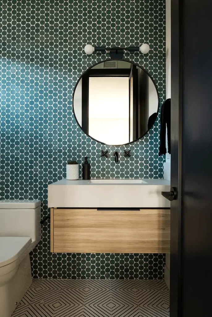 Contemporary bathroom by Grace Blu with teal tile, round mirror, wood vanity, and matte black fixtures.