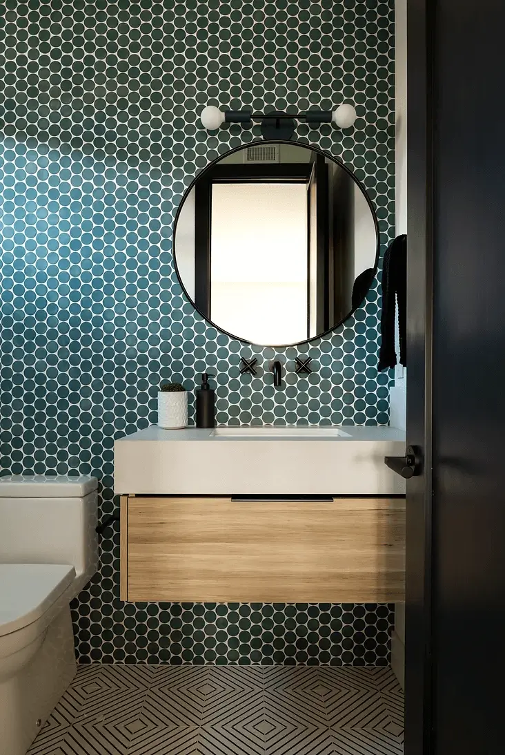 Contemporary bathroom by Grace Blu with teal tile, round mirror, wood vanity, and matte black fixtures.