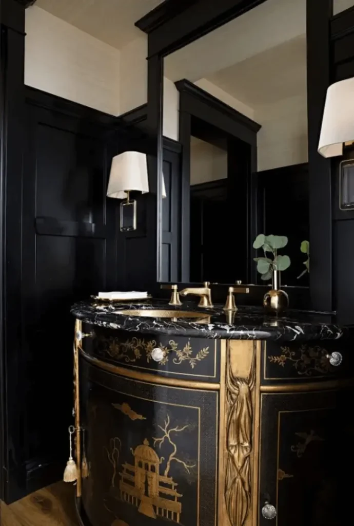 Dramatic powder room with black paneled walls, black and gold vanity, marble countertop, and brass fixtures.