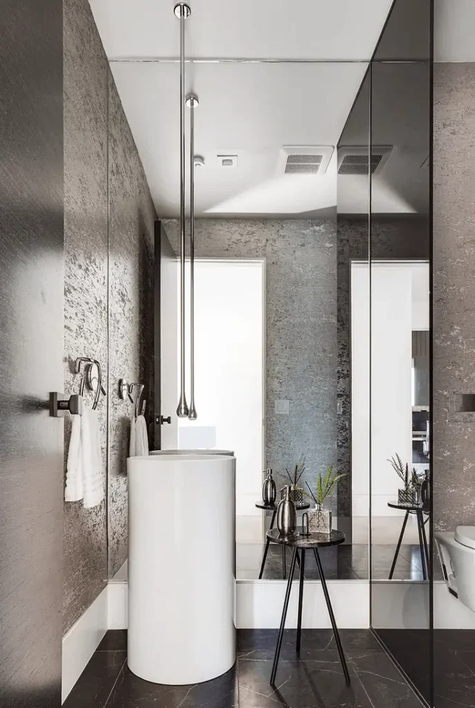 Modern powder room with white pedestal sink, mirrored walls, metallic wallpaper, and black marble floors.