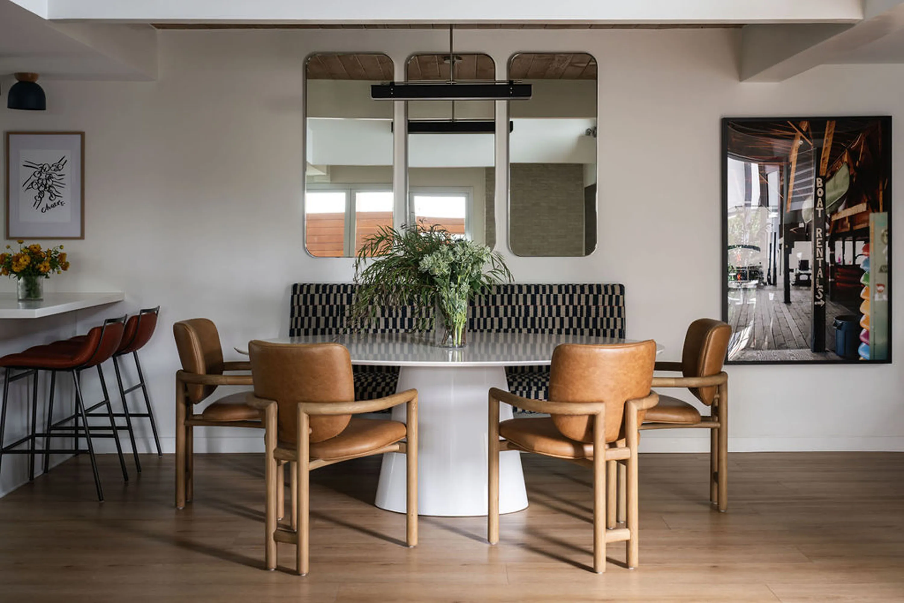 Dining area with a white pedestal table, tan leather chairs, checkered banquette and arched mirrors
