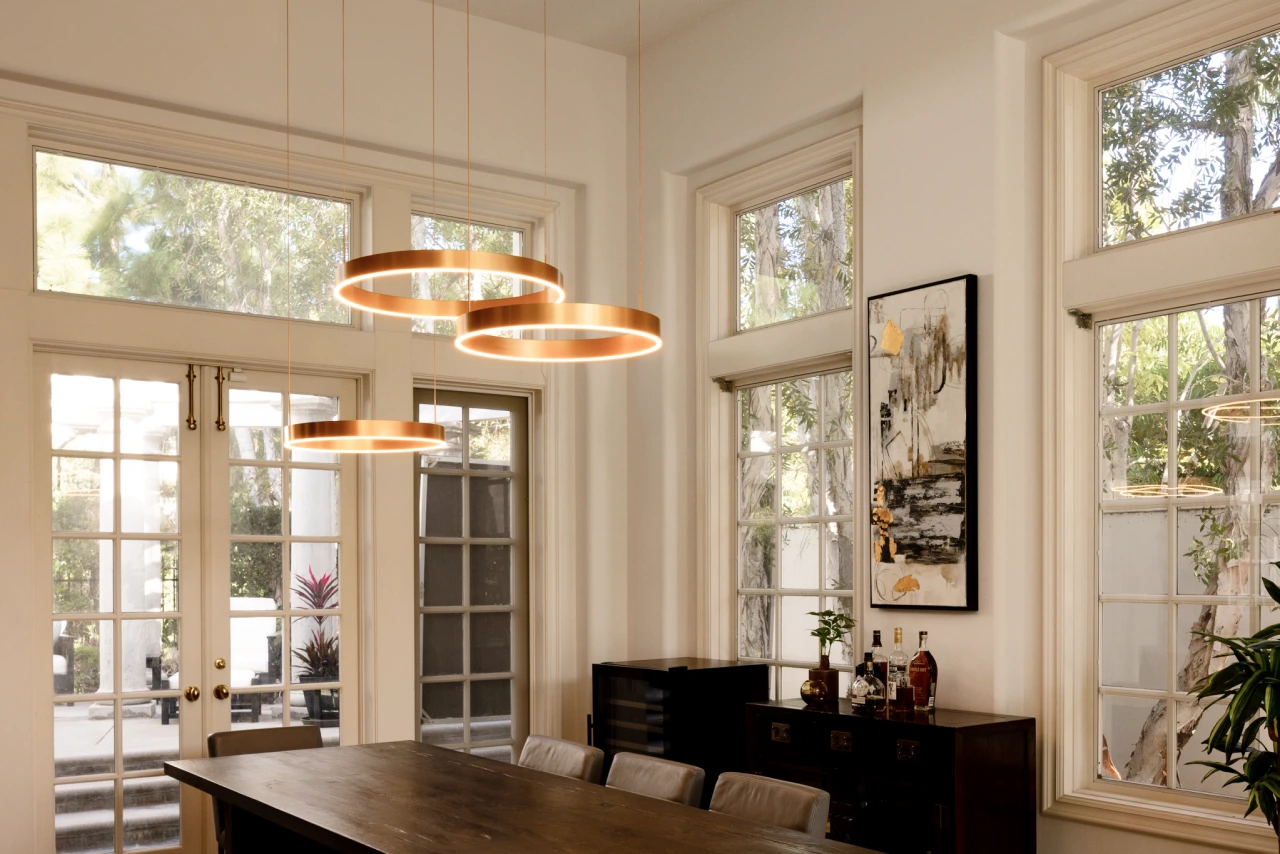 Charlotte dining room with double-height ceilings, gold ring pendants, and dark wood table.