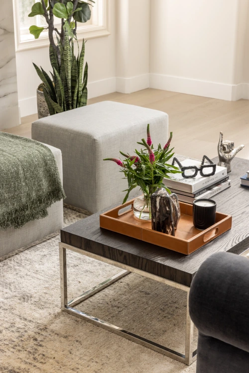 Living room detail from Grace Blu’s Interior Design Project Charlotte featuring a dark gray ottoman, textured rug, and a wood tray with fresh florals, with two grey bean bag chairs.