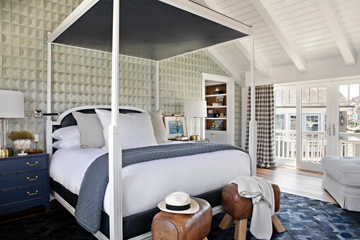 Coastal bedroom with canopy bed, elegant patterns around room and warm leather ottomans at foot of bed