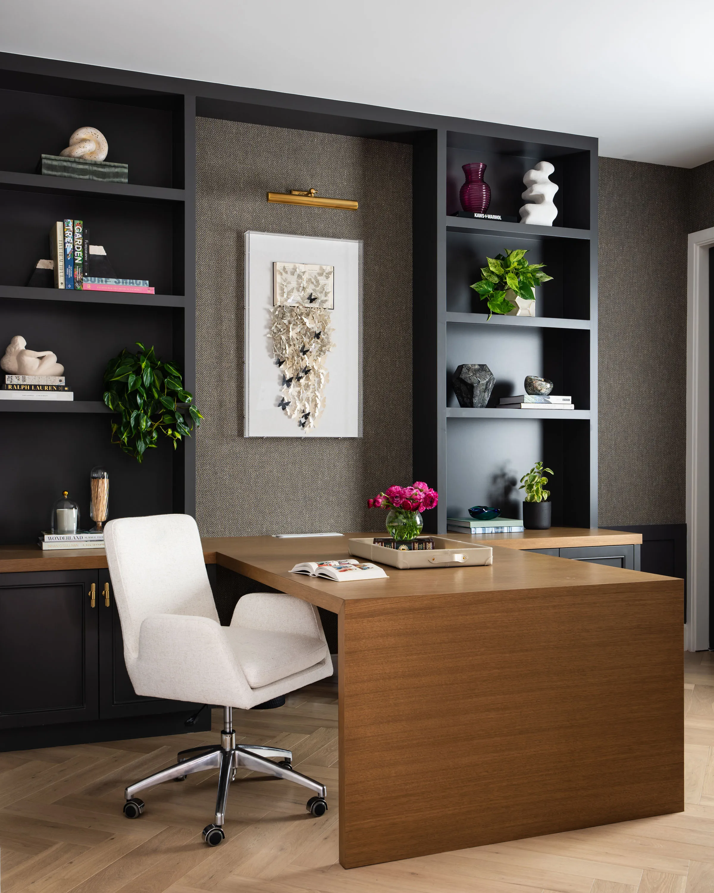 Home office with a walnut desk, black built-in shelving and a textured artwork