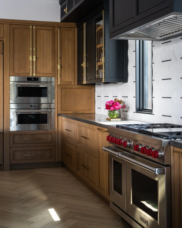 Kitchen with bold black cabinets, chairs and island featuring gold accents, wooden cabinets and white marble wall