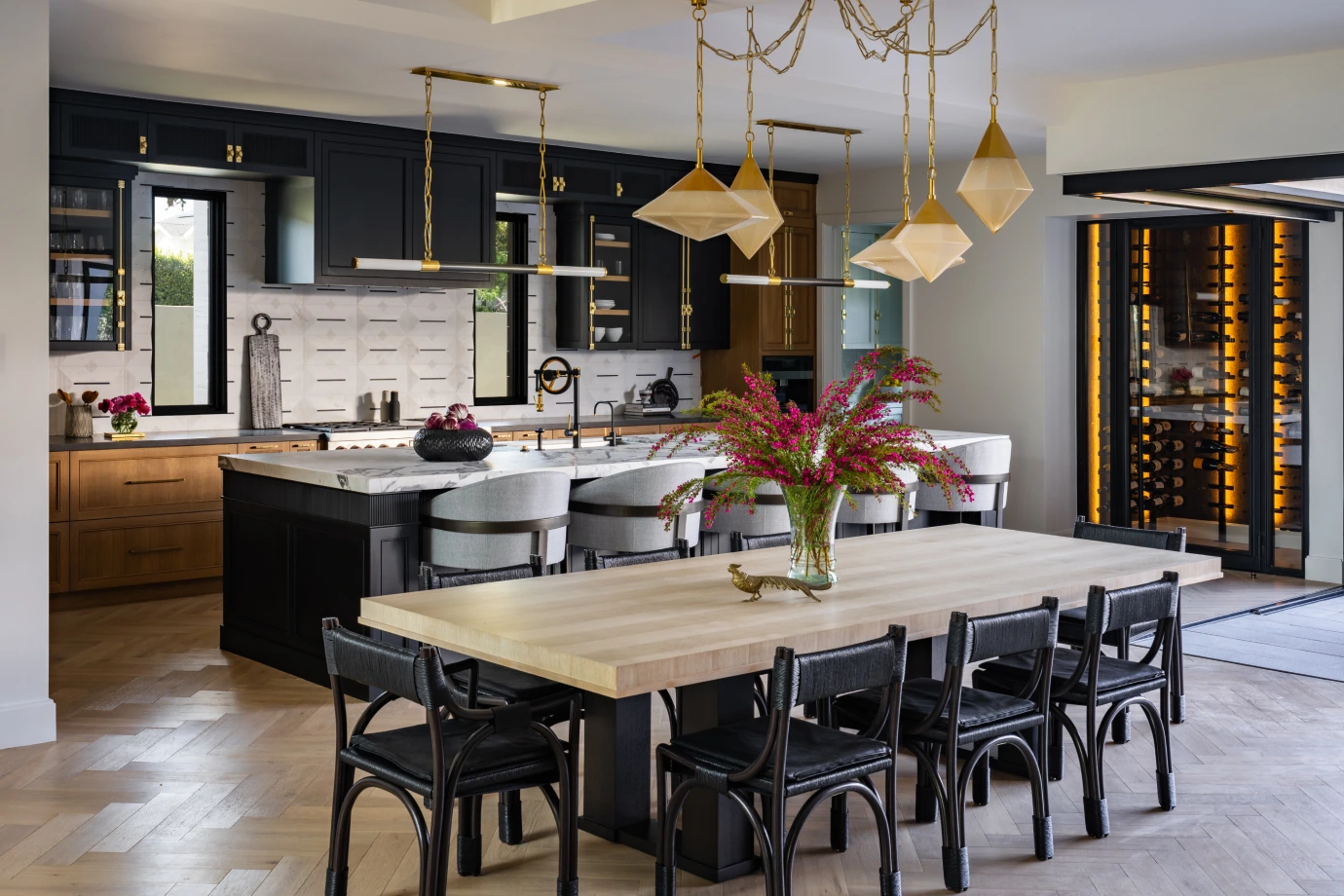 Kitchen and dining room from Grace Blu's Herringbone Habitat Interior Design project with black cabinets, chairs, and kitchen island. Featuring gold accents and wooden cabinets with a white marble wall.