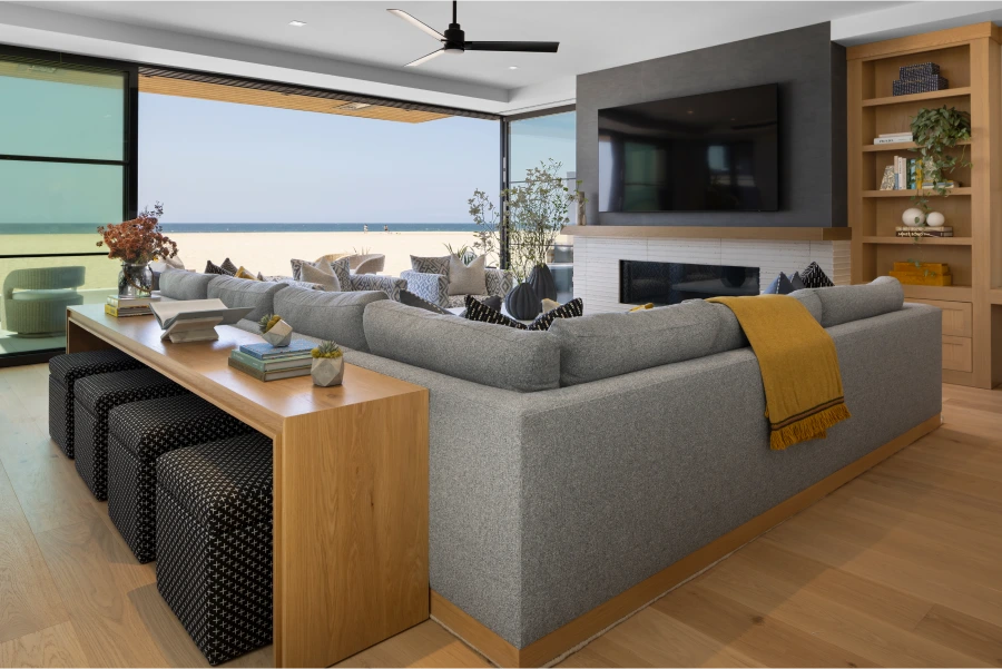 oceanfront living room with yellow blanket and pillow on couch, floor to ceiling glass doors opening to sand