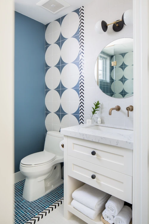 Bathroom with bold blue-and-white circular tile, round mirror, white vanity, and brass fixtures.