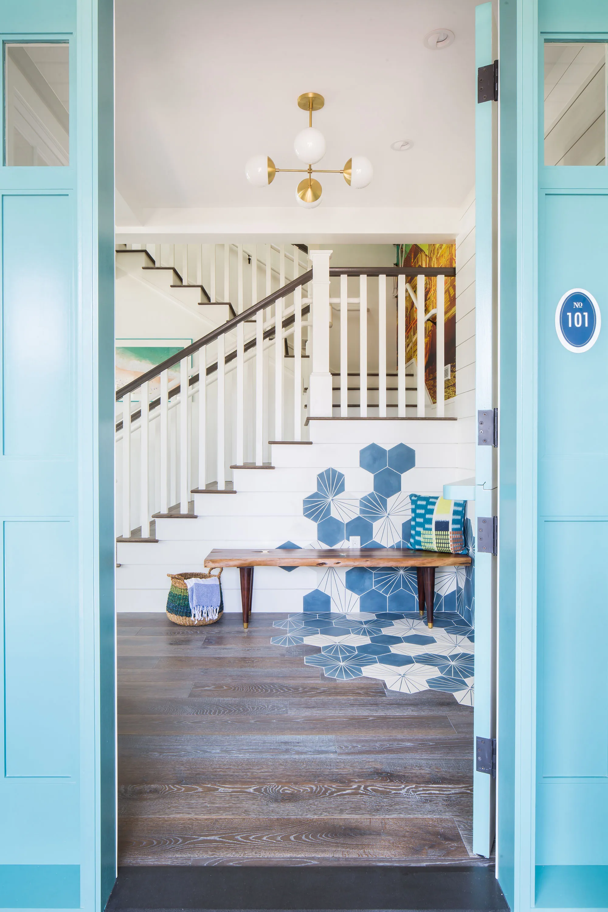 Entry viewed through turquoise double doors, with hexagon floor tile and a live-edge bench