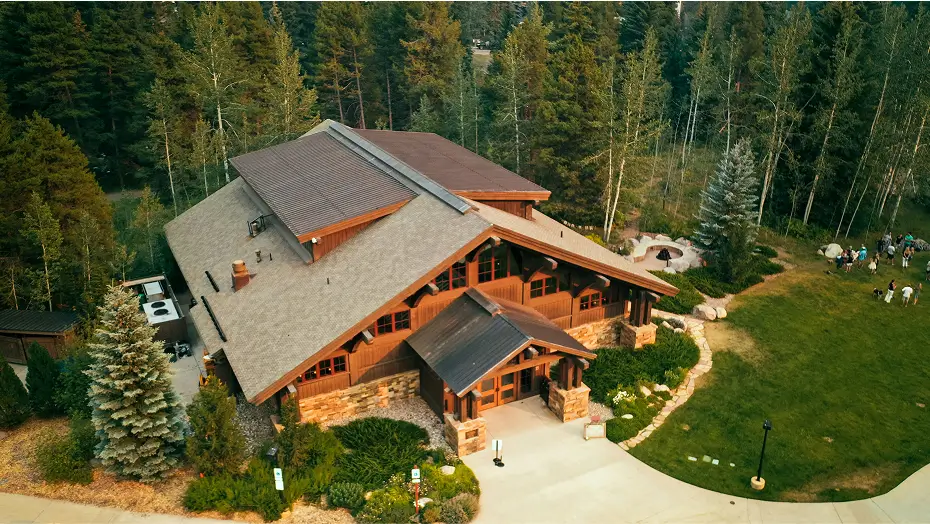 Aerial view of a large wooden cabin from Grace Blu's Big Sky Design Project in the green forest with tall trees surrounding it