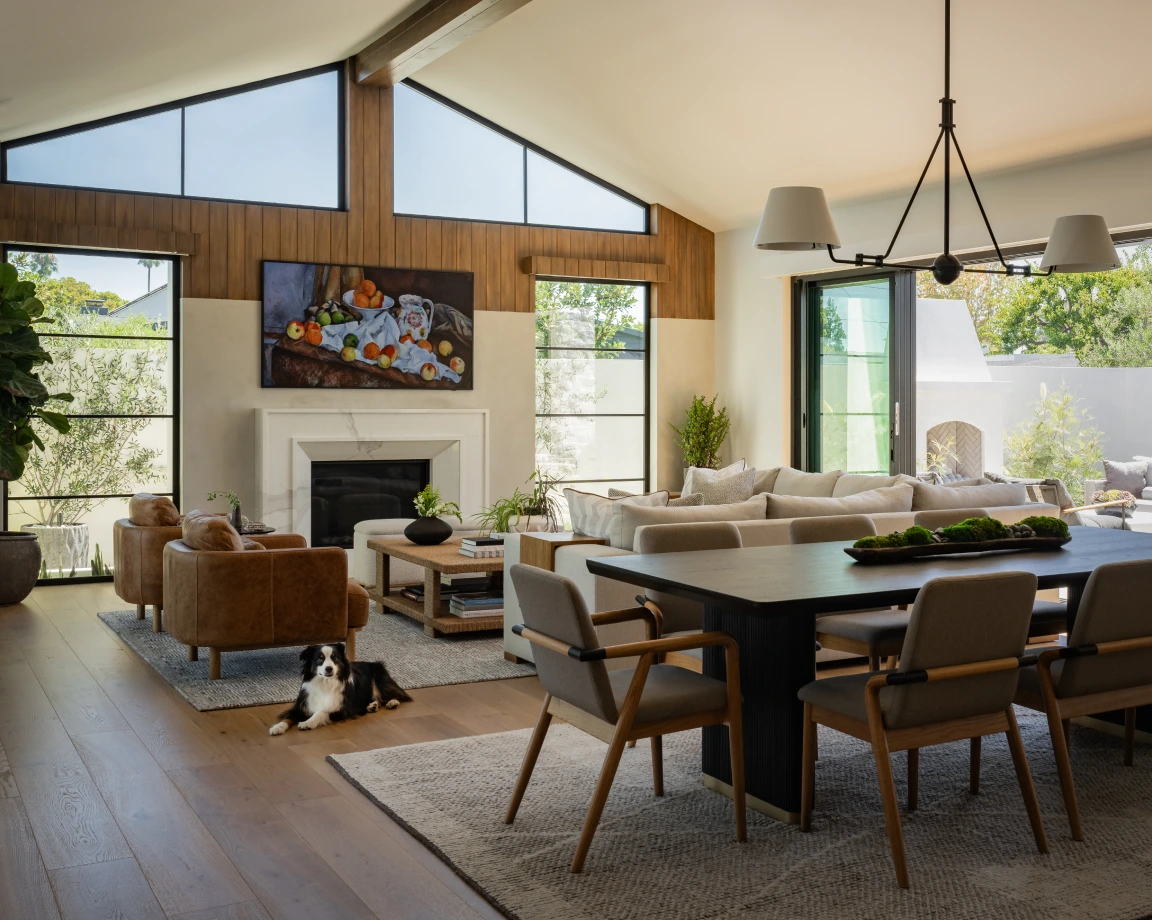 Grace Blu Rattan Galore living-dining space with vaulted ceiling, fireplace, neutral sectional, and black table with taupe chairs.