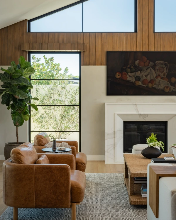 Fireplace with wood paneling, clerestory windows, white mantle, and brown leather lounge chairs.