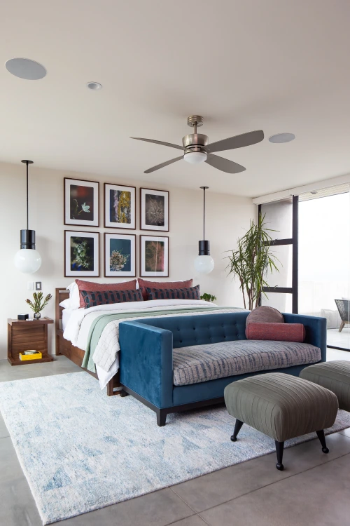 Bedroom from Grace Blu's Interior Design Project Sommet du Monde featuring a queen sized bed with a dark blue sofa in front with six colorful frames hanging on the wall behind