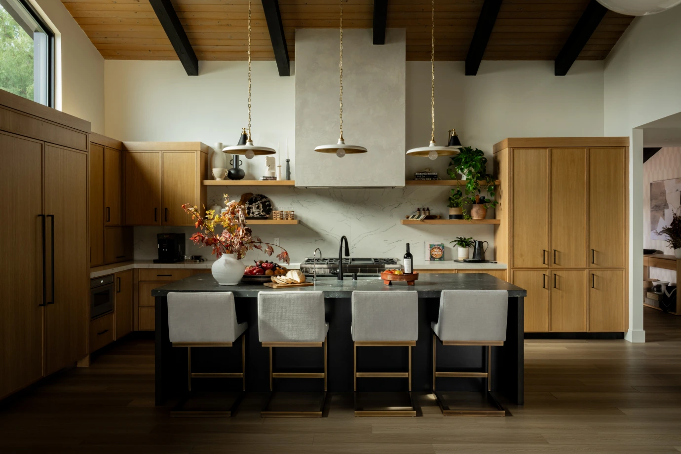 Kitchen island from Grace Blu’s Interior Design Project Travertine with a black island table and fall floral arrangement and hanging lights.