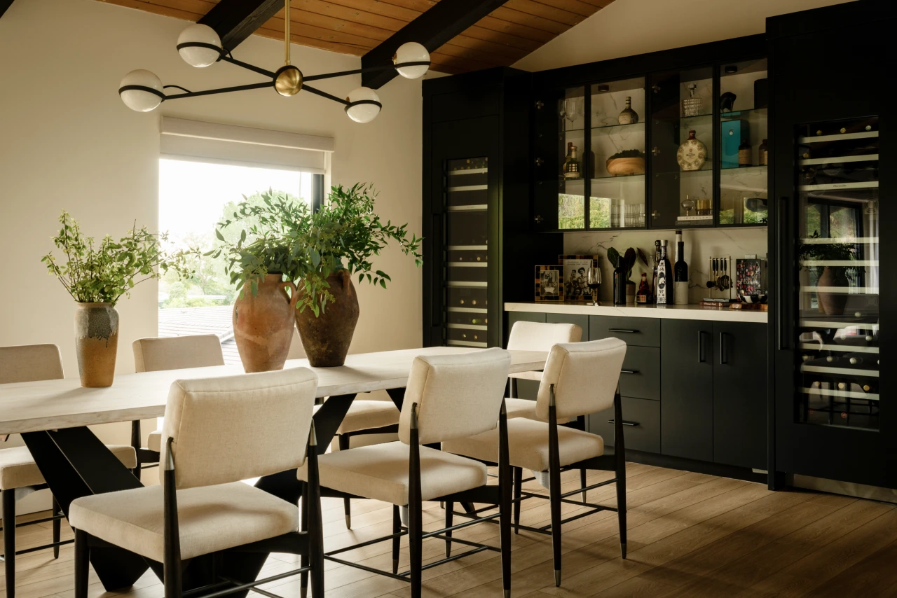 Travertine dining with long table, wood ceiling, pottery, and bar view.
