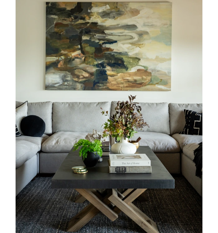 Living room with gray sofa, abstract art, and black coffee table styled with books and plants in a vase.