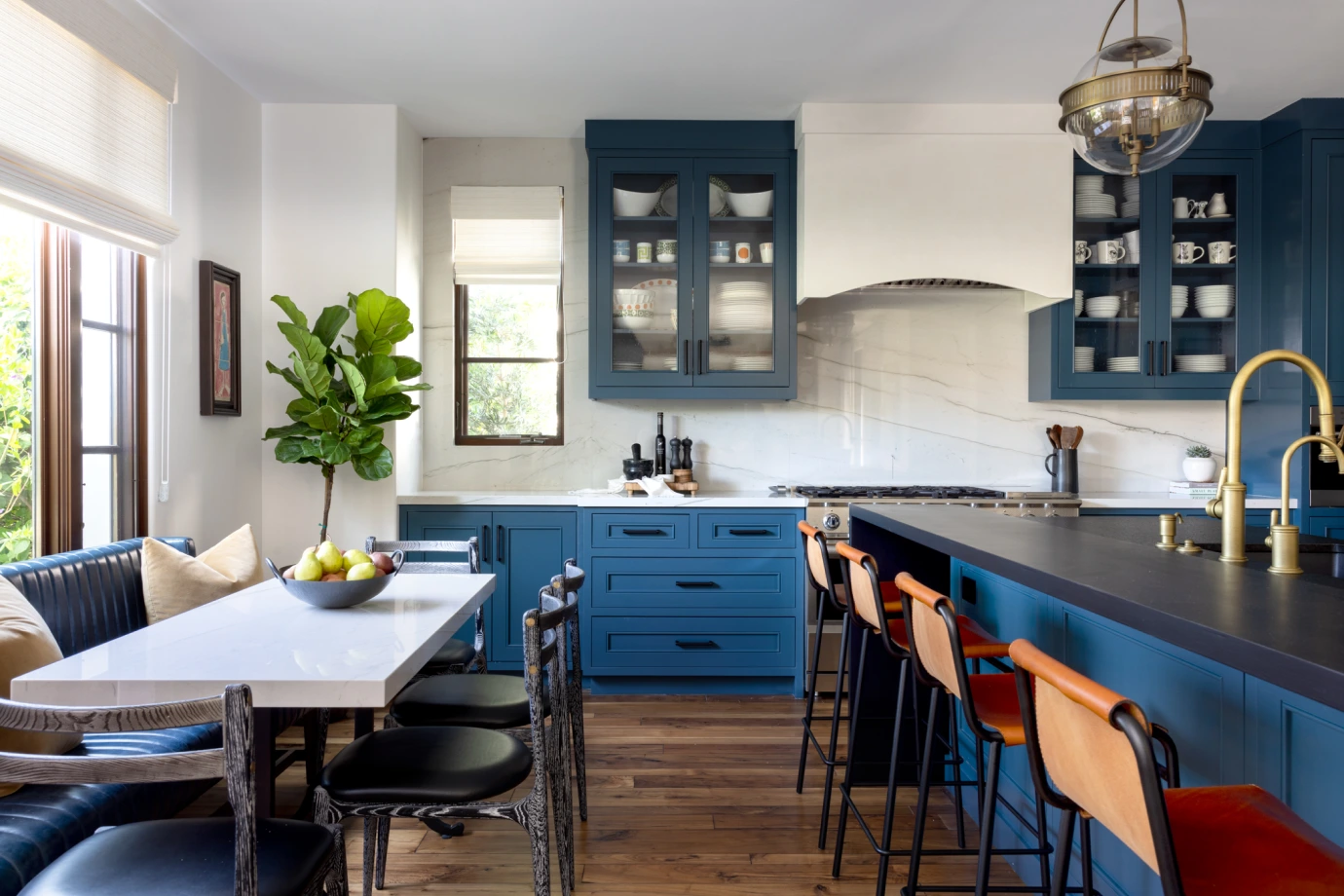 Grace Blu Via Jucar kitchen with blue cabinets, white marble surfaces, orange island stools, and blue sofa at dining table.