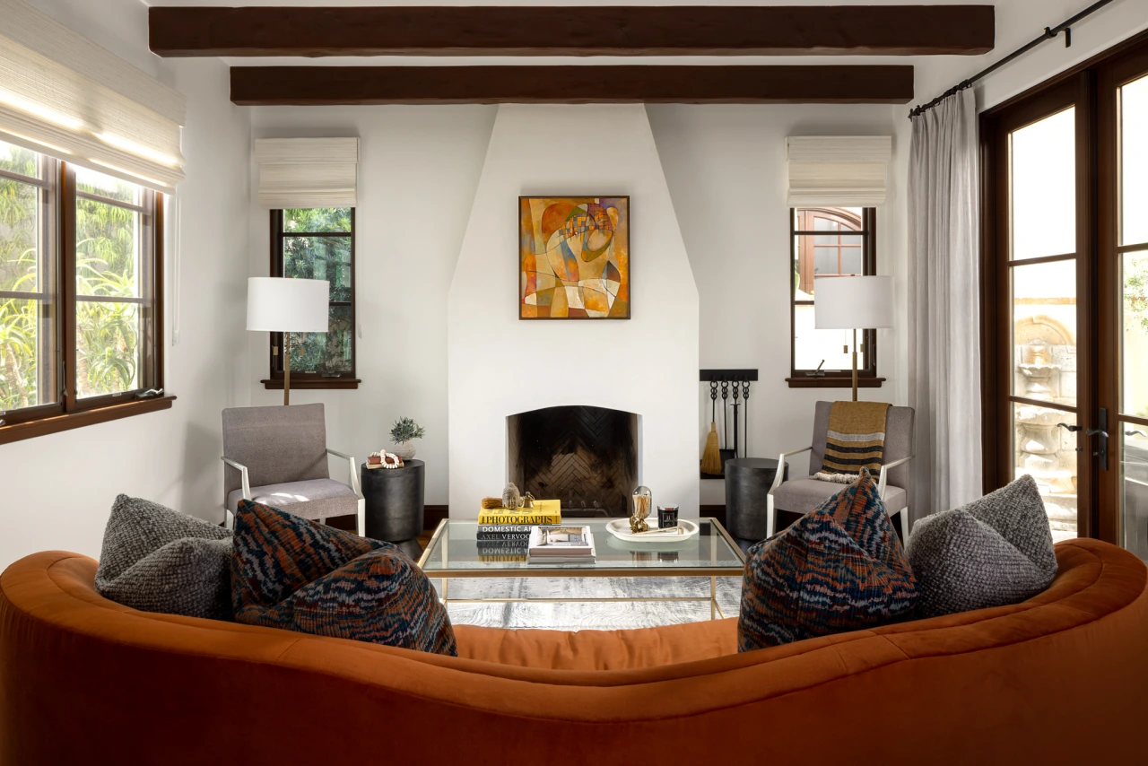 Grace Blu Via Jucar living room with white stucco fireplace, abstract art, orange sofa, and metallic-accented coffee table.