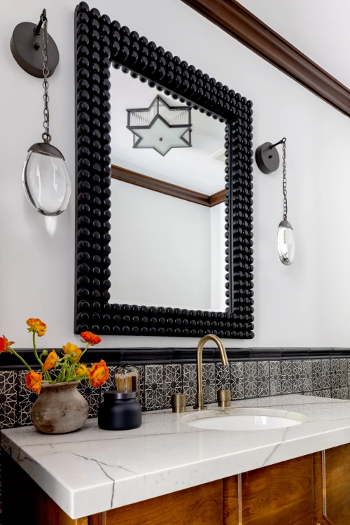 Via Jucar bathroom sink with black lego-frame mirror and counter decorated with yellow and orange flowers by Grace Blu.