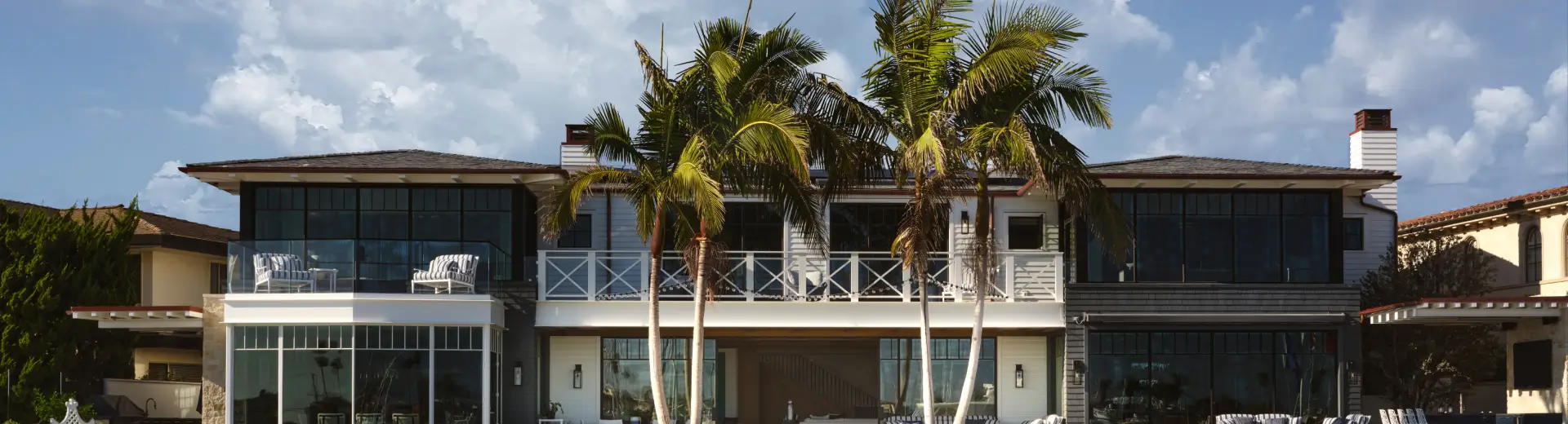 Modern beachfront home with palm trees and outdoor seating facing the ocean.