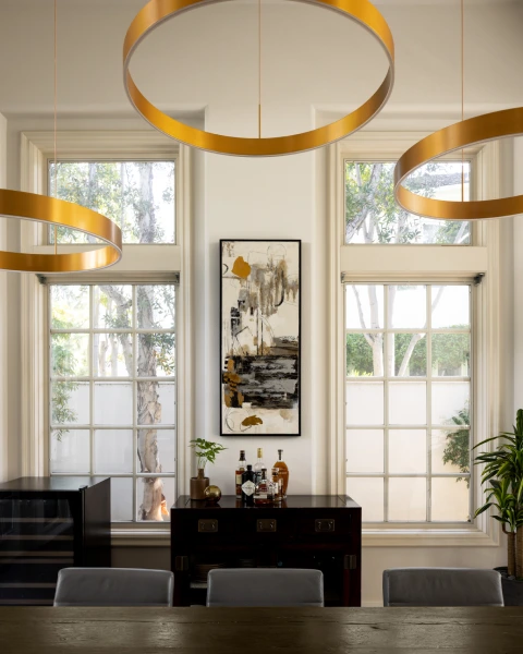 Charlotte dining with layered gold ring lights, tall windows, and black dresser.